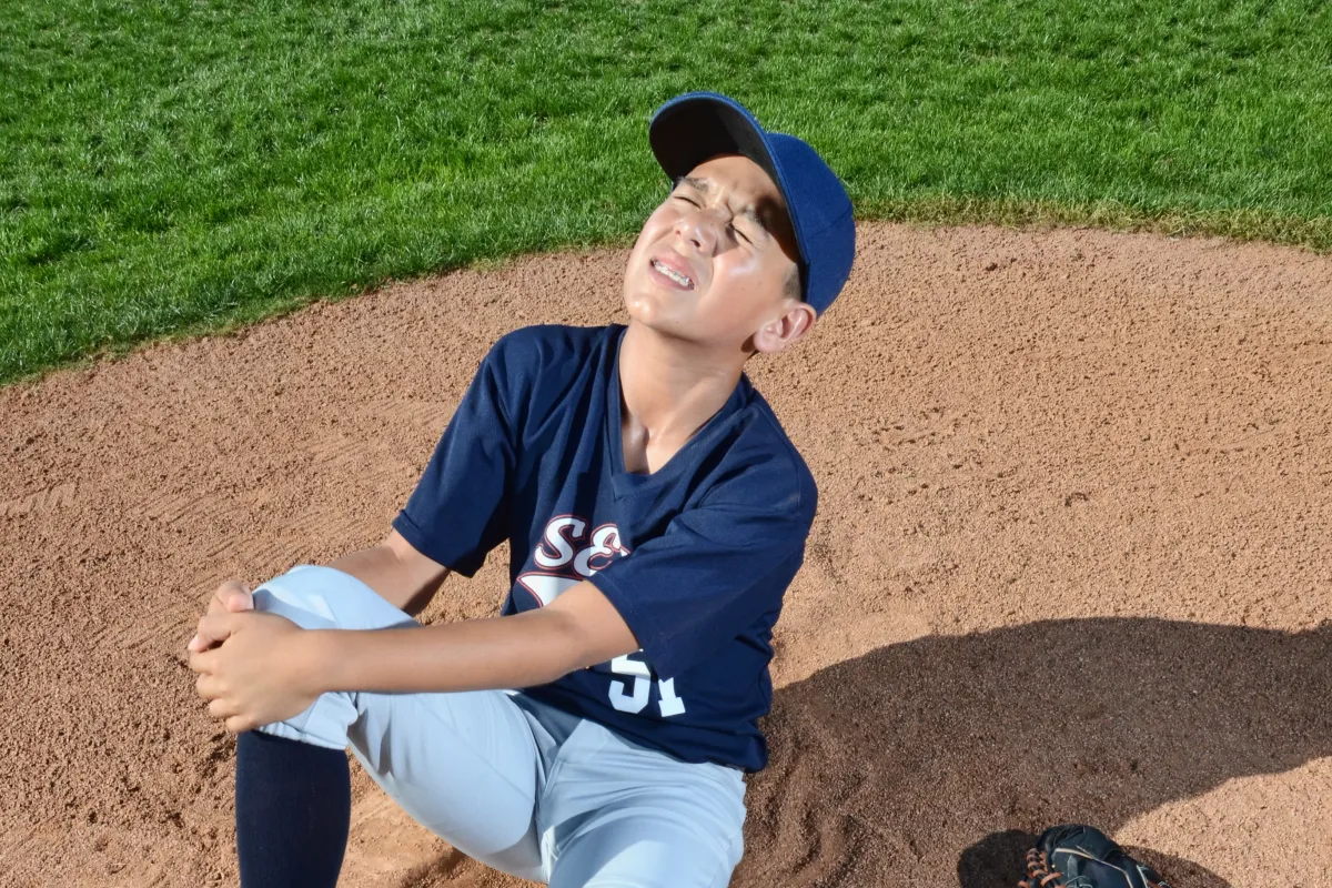 マウンドで脚を押さえて痛がる少年野球の選手